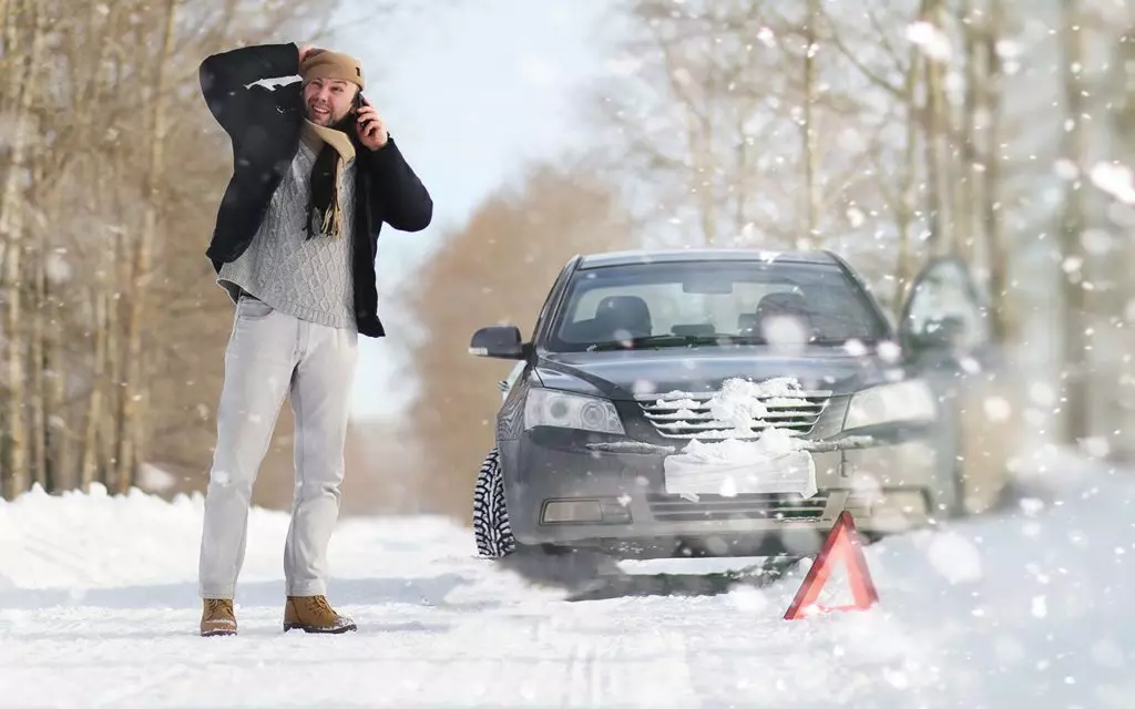 A man near a broken car on a cold winter day